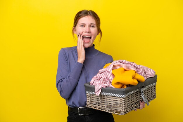 Young english woman holding a clothes basket isolated on yellow background with surprise and shocked facial expression