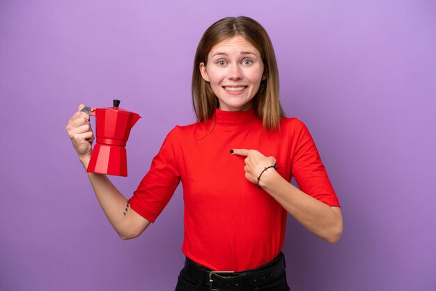 Young English woman holding coffee pot isolated on purple background with surprise facial expression