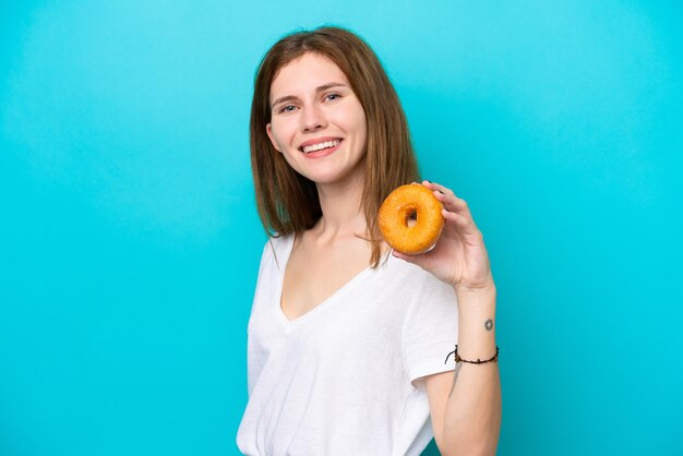 Young English woman holding a donut over isolated blue background smiling a lot