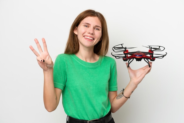 Young English woman holding a drone isolated on white background happy and counting three with fingers