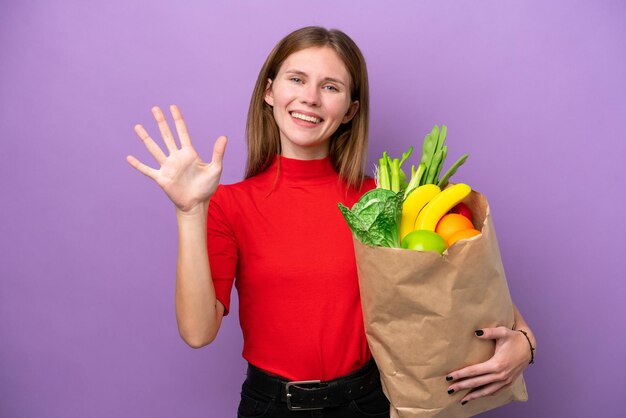 Young english woman holding a grocery shopping bag isolated on purple background counting five with fingers