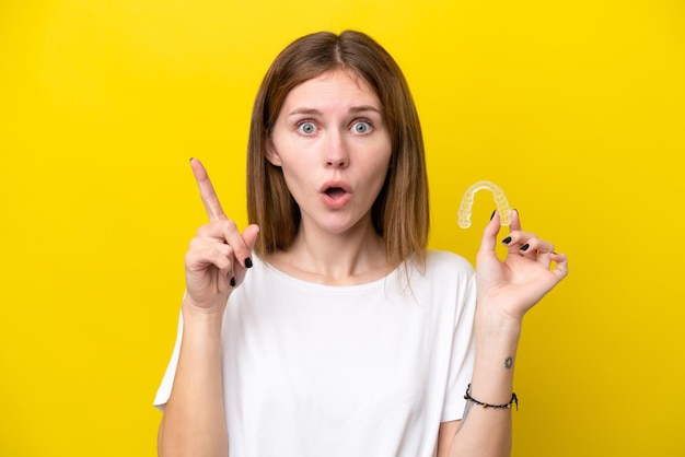 Young english woman holding invisible braces intending to realizes the solution while lifting a finger up