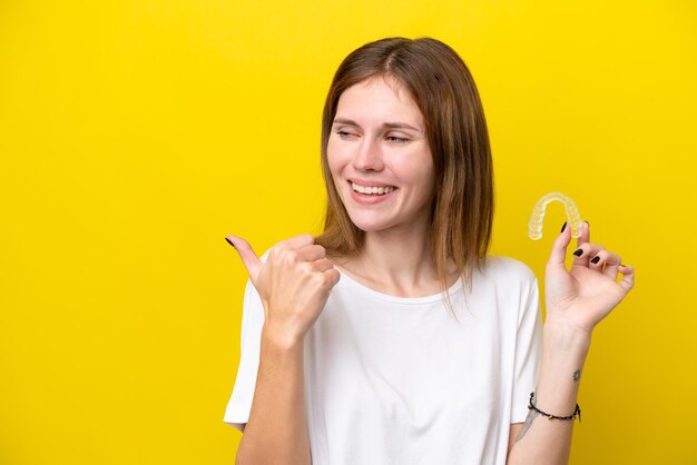 Young English woman holding invisible braces pointing to the side to present a product