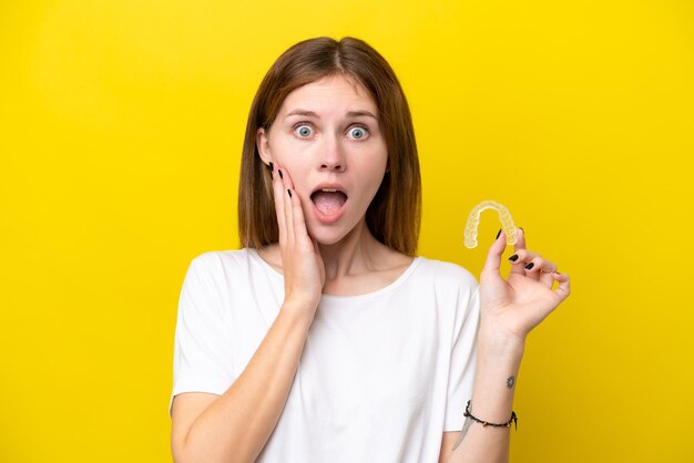 Young english woman holding invisible braces with surprise and shocked facial expression