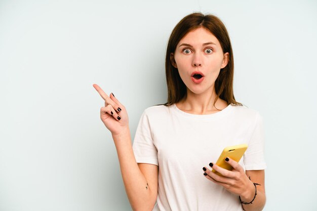 Foto giovane donna inglese che tiene il telefono cellulare isolato su sfondo blu che indica il lato