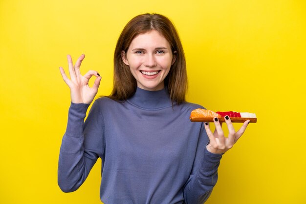 写真 指でokサインを示す黄色の背景に刺身を保持している若いイギリス人女性