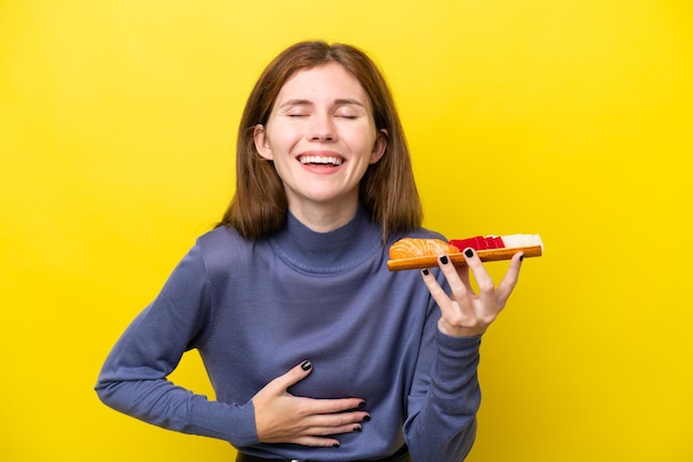 Young english woman holding sashimi isolated on yellow background smiling a lot