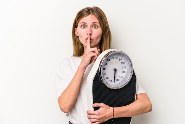 Young English woman holding a scale isolated on white background keeping a secret or asking for silence.