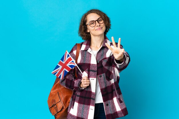 幸せな青いスペースに分離されたイギリスの旗を保持し、指で3を数える若いイギリス人女性