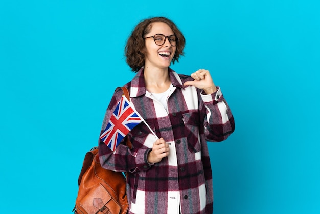 Young English woman holding an United Kingdom flag isolated on blue space proud and self-satisfied