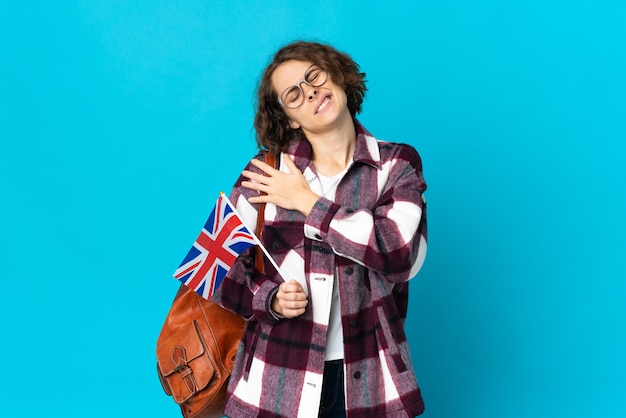 Young English woman holding an United Kingdom flag isolated on blue wall suffering from pain in shoulder for having made an effort