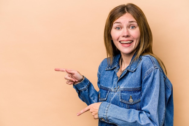 Young English woman isolated on beige background excited pointing with forefingers away