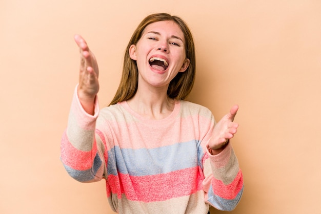 Young English woman isolated on beige background feels confident giving a hug to the camera