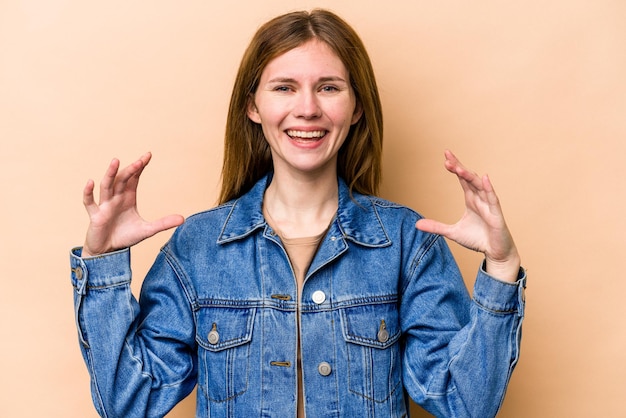 Young English woman isolated on beige background holding something with palms offering to camera