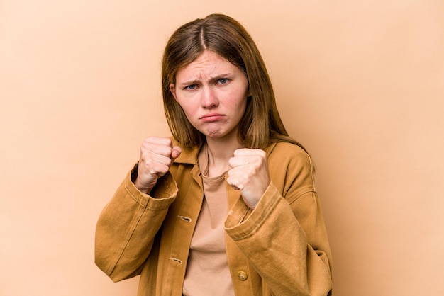 Young English woman isolated on beige background showing fist to camera aggressive facial expression