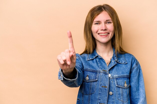 指でナンバーワンを示すベージュの背景に分離された若いイギリス人女性