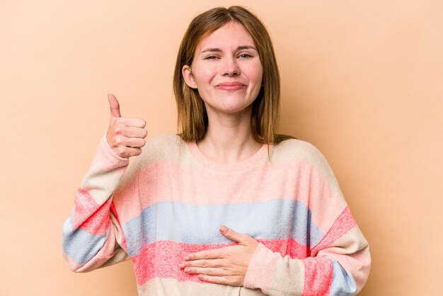 Photo young english woman isolated on beige background touches tummy smiles gently eating and satisfaction concept