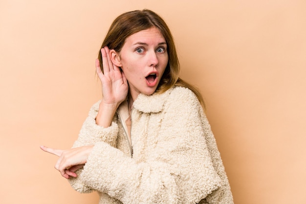 Young English woman isolated on beige background trying to listening a gossip