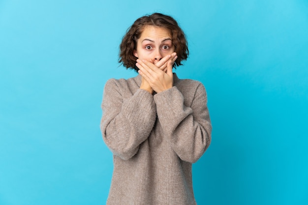 Young English woman isolated on blue background covering mouth with hands