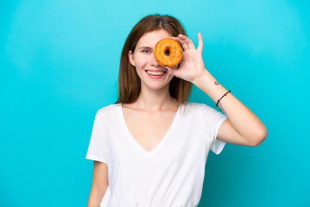 Young English woman isolated on blue background holding a donut and happy