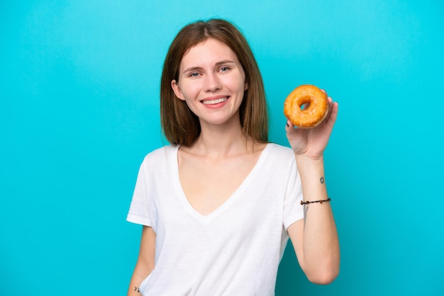 Молодая англичанка, изолированная на синем фоне, держащая пончик и счастливая