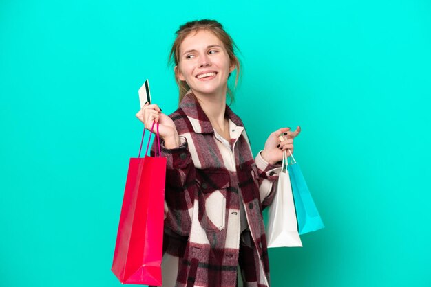 Young English woman isolated on blue background holding shopping bags and a credit card