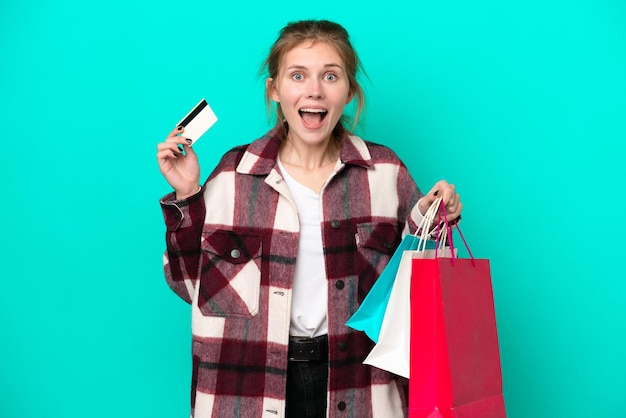 Young english woman isolated on blue background holding shopping bags and surprised