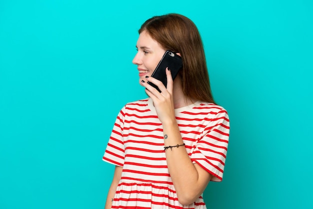Foto giovane donna inglese isolata su sfondo blu che mantiene una conversazione con il telefono cellulare con qualcuno