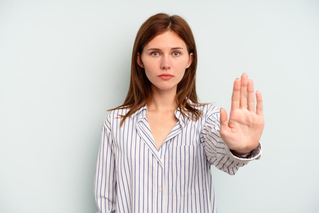 Young English woman isolated on blue background standing with outstretched hand showing stop sign, preventing you.