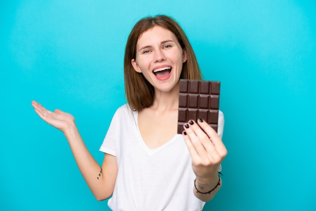 Giovane donna inglese isolata su sfondo blu che prende una tavoletta di cioccolato e sorpresa