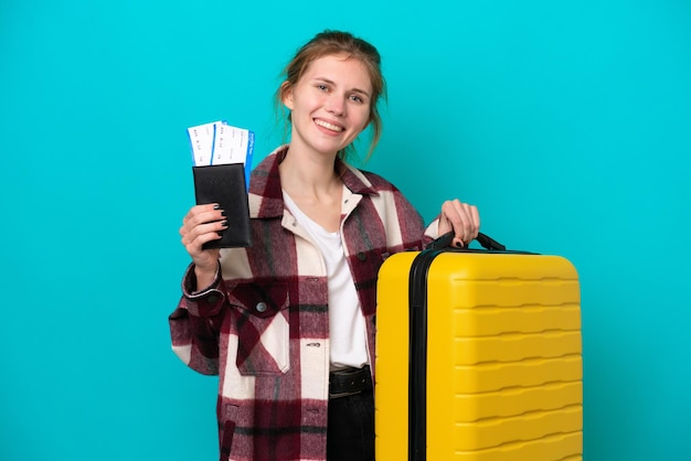 Young English woman isolated on blue background in vacation with suitcase and passport