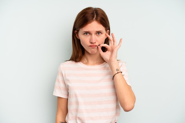 Young English woman isolated on blue background with fingers on lips keeping a secret.