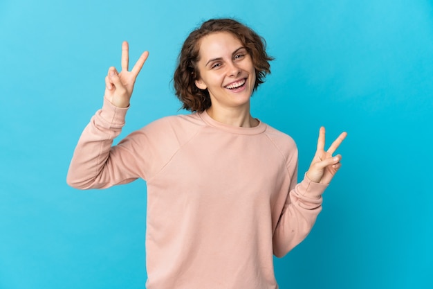 Young English woman isolated on blue space showing victory sign with both hands