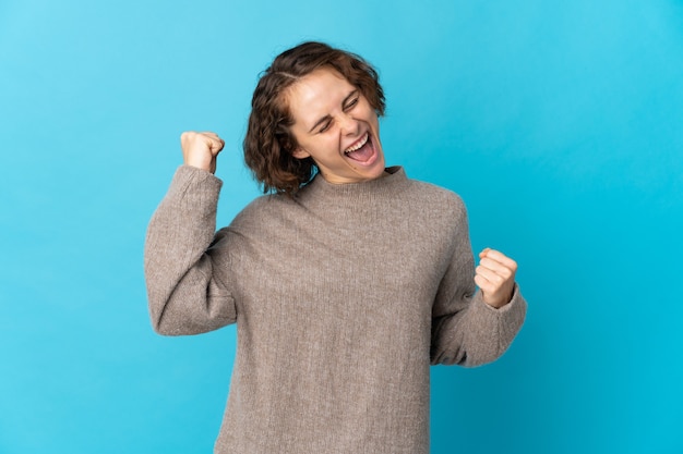 Young English woman isolated on blue wall celebrating a victory