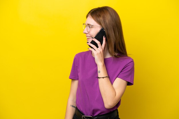 Фото Молодая англичанка изолирована на желтом фоне, разговаривая с кем-то по мобильному телефону