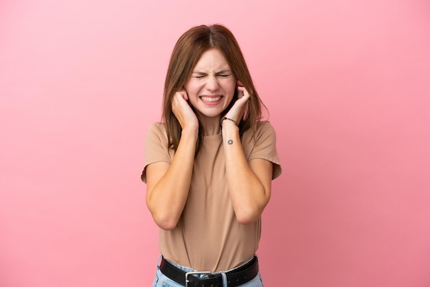 欲求不満と耳を覆っているピンクの背景に分離された若いイギリス人女性