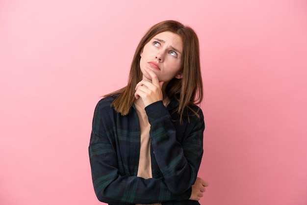 Young English woman isolated on pink background having doubts