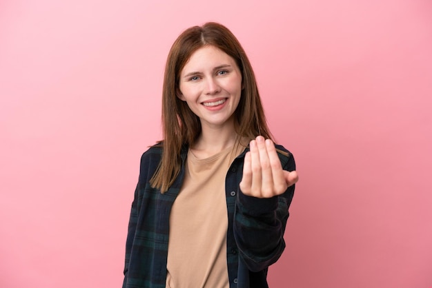 ピンクの背景に孤立した若いイギリス人女性が手で来るように誘うあなたが来て幸せ