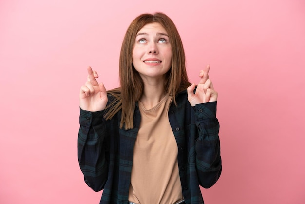 Young English woman isolated on pink background with fingers crossing and wishing the best