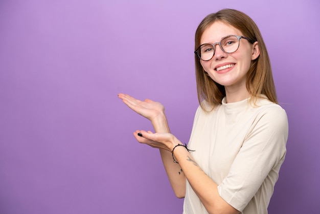 紫色の背景に孤立した若いイギリス人女性が来て招待するために手を横に伸ばします