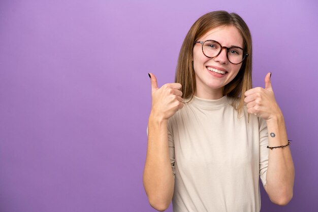 親指を立てるジェスチャーを与える紫色の背景に分離された若いイギリス人女性