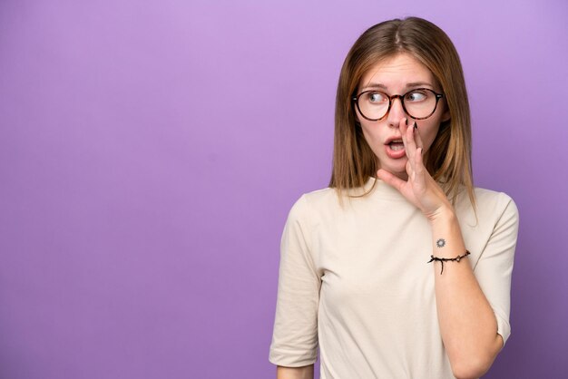 Young english woman isolated on purple background whispering something with surprise gesture while looking to the side