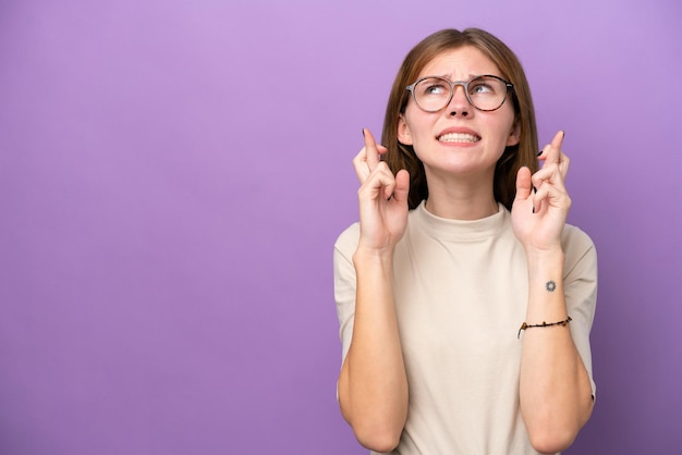 指が交差し、最高を願って紫色の背景に分離された若いイギリス人女性