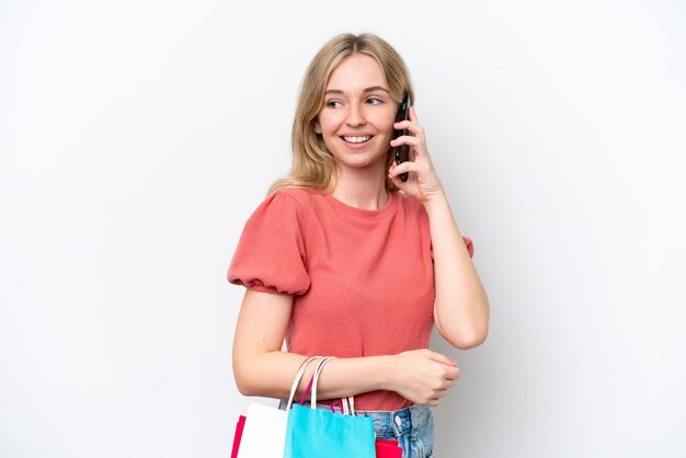 Young English woman isolated on white background holding shopping bags and calling a friend with her cell phone