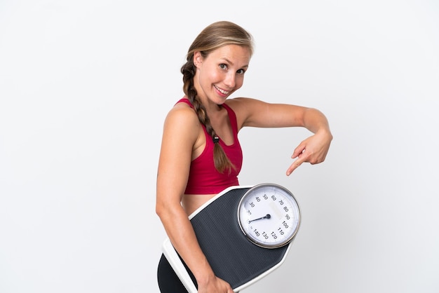 Young English woman isolated on white background holding a weighing machine and pointing it