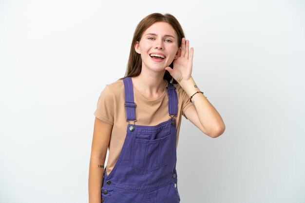 Young English woman isolated on white background listening to something by putting hand on the ear