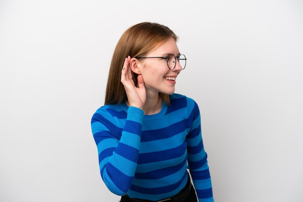 Young English woman isolated on white background listening to something by putting hand on the ear