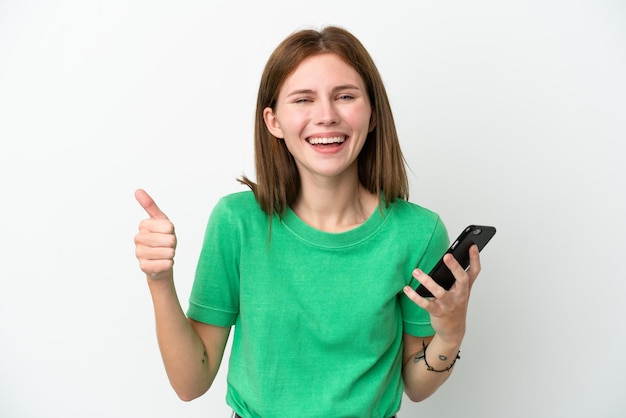 Young English woman isolated on white background using mobile phone while doing thumbs up