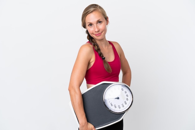 Young English woman isolated on white background with arms at hip and holding weighing machine