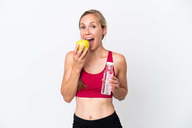 Young English woman isolated on white background with a bottle of water and eating an apple